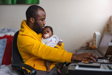 Man holding his newborn baby girl and working with laptop at home
