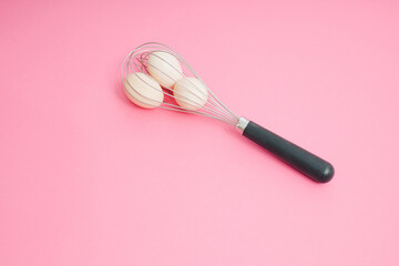 Whisk and raw eggs on pastel pink. Light banner background, copy space for text. Culinary mixer,...