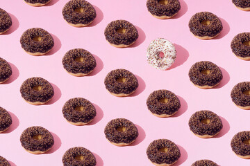 Fototapeta premium Arranged ring donuts with chocolate and white glaze and small colorful crumbs on a pink pastel background. Pattern.