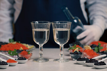 Waiter pouring champagne or white wine from a bottle into glasses at buffet table while tasting...