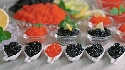 Many red and black caviar in dishes. Glass bowl and white spoons with elite salmon caviar and black...
