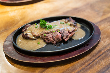Grilled Juicy steak medium rare beef with herbs and spices on pan hot topped with black pepper sauce on wooden table.
