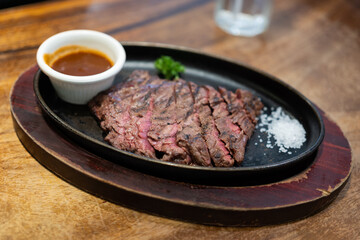 Grilled Juicy steak medium rare beef with herbs and spices on pan hot served with salt and brown sauce on wooden table.
