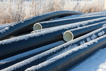 Plastic water pipes. Black PVC tubes plastic pipes stacked on white snow background. Heating houses in winter.