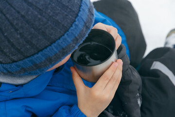Child hands holds a cup. Child drinking a cup of tea on the street while walking. Winter walk