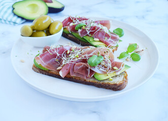 Whole grain bread sandwiches with slices of avocado, prosciutto or jamon, germinated seeds and herbs. Clean eating, healthy breakfast. Top view