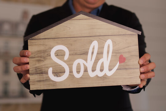 person holding a sold sign in the shape of a house real-estate agent  
