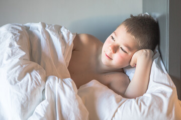 Kid 7 year old lying on bed, Sleepy child waking up the morning in his bed room with morning light, sad boy lies on a bed in the room