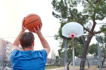 Young player throwing to the basket. Unrecognizable Caucasian man with his back turned playing on a basketball court.
