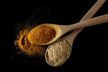 Turmeric (Curcuma) and ginger powder piles in wooden spoon isolated on black, top view 