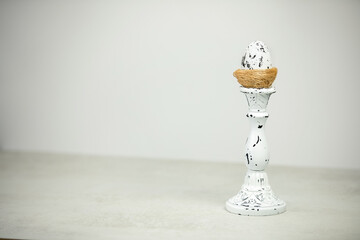 A decorative nest with a white egg on a spotted candlestick on a white background
