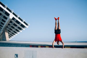 Strength male acrobat with muscular body doing handstand exercise during leisure at urban setting,...