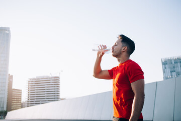 Thirsty athletic man holding bottle for cold refreshing after energetic outdoors jogging around...