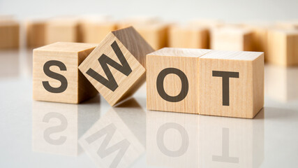 four wooden blocks with the letters SWOT on the bright surface of a gray table, business conceptual word collected of of wooden elements with the letters