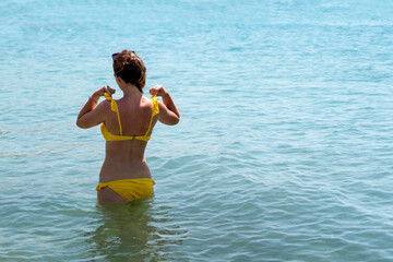 young girl standing in sea water on the summer beach, view from behind