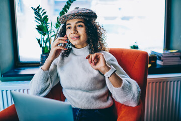 Young female with modern laptop computer making mobile conversation via cell application, skilled...