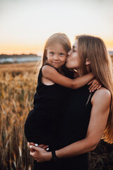 Cute girl hugging her mother on a golden wheat field on summer sunset.