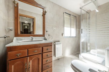 Toilet with glass shower cubicle, white porcelain sink with marble top in wooden cabinet in vacation rental apartment