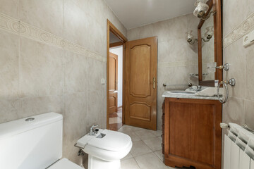 Toilet with oak door and beige tiles, white porcelain sink with marble top in wooden cabinet in vacation rental apartment