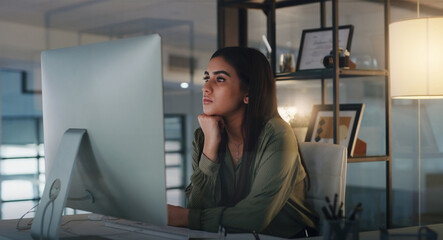 Another bright idea will hit her soon. Shot of a young businesswoman looking thoughtful while working on a computer in an office at night. © Norman L/peopleimages.com