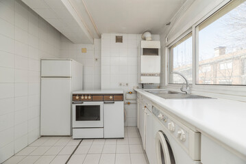 White vintage kitchen with window with views, white appliances and stoneware floors of the same color, butane metal kitchen with oven and refrigerator next to it