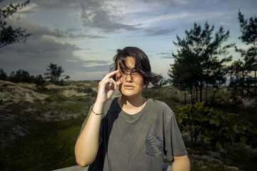 Young male gender fluid female on a beach on a stormy day with the dunes and the sea in the...