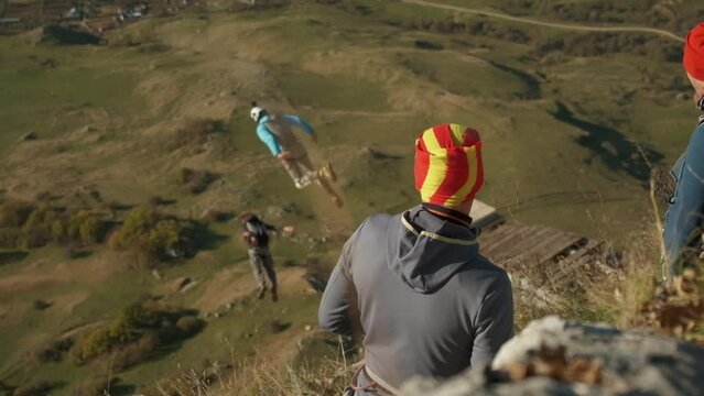 people watch as two men jump off a cliff with a parachute