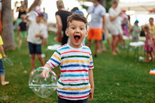 emotional child with soap bubbles. An emotional boy with a big bubble. Summer weekend, recreation, children's animation in the park in the fresh air, animation program with soap bubbles.