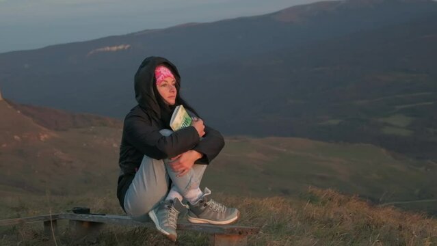 a girl looks at the sunset, holding a book in her hands against the background of mountains