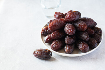 Medjoul dates in a white plate and glass of water on a gray background. Close up. - 491919495
