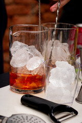 Negroni classic cocktail. Close up shot of bartender hand stirring a negroni cocktail. Glass of drink on counter with orange peal. Bartender hand making negroni cocktail