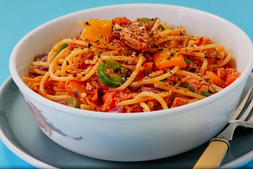 Bowl of tuna bolognese garnished with seasoning,shot on a blue background.