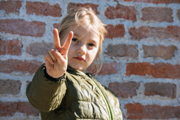 Child refugee showing peace sign behind a metal fence. Social problem of war migrants.