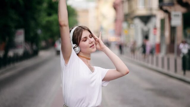 Beautiful sexy woman with tattoo wearing blank white t-shirt and jeans dancing on a street. Young pretty hipster girl in wireless headphones having fun, listening music and dancing on the street