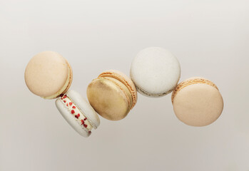 White, yellow, gold macaron cookies flying, falling in motion or levitating. Colorful, sweet small French macaroon cakes. Light beige background. Broken cut, bitten parts, halves. High quality photo