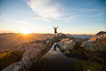 Hiker standing on summit, reaching for the sky, success.