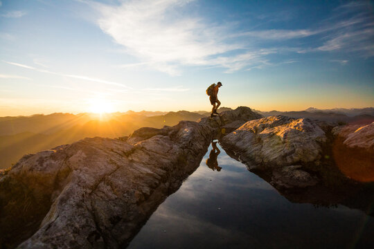 Backpacker hiking over rocky mountain terrain at sunset.