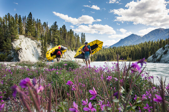 Paddlers carrying packrafts beside river in the mountains.