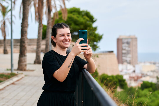 Young woman smiles and takes a picture with her phone in a park