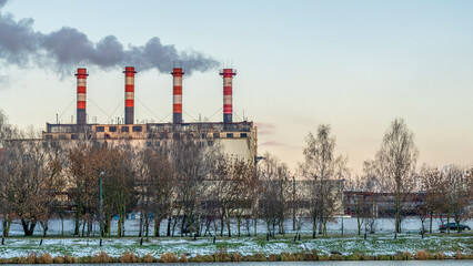 Obraz premium Power station with reservoir in winter. Beautiful seaside winter sunset with a smoking factory chimney.