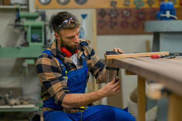 Young handsome caucasian carpenter working with clamps in workshop