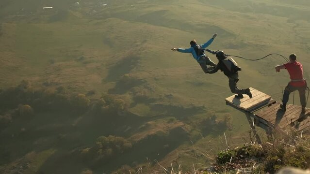 two men jump from a cliff, one with a parachute and the other with a rope, a man jumps from a mountain