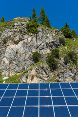 Solar photovoltaic panels against the backdrop of rocky mountains covered with green plants and trees - 491924082
