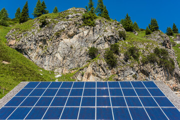 Solar photovoltaic panels against the backdrop of rocky mountains covered with green plants and trees - 491924085