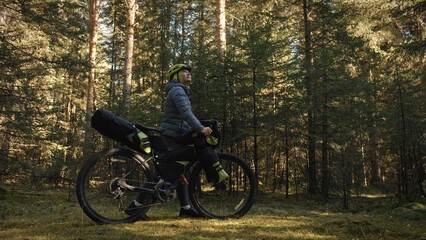 The woman travel on mixed terrain cycle touring with bike bikepacking outdoor. The traveler journey with bicycle bags. Stylish bikepacking, bike, sportswear in green black colors. Magic forest park.