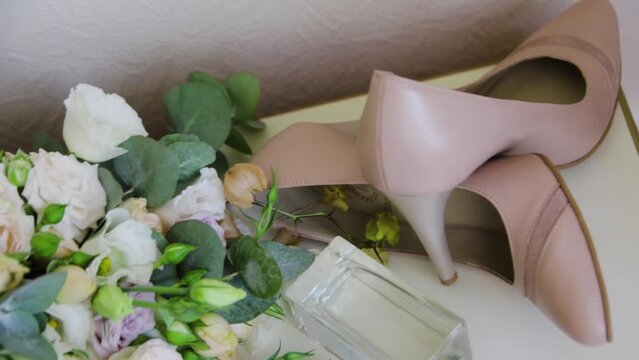 Bride's wedding accessories close-up. Beige high heel shoes, bouquet of light flowers with ribbons and bottle of perfume