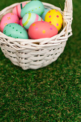 Vertical Easter background with colorful yellow, pink, blue Easter eggs in woven basket and green grass. Top view with copy space. Easter holidays social media background.