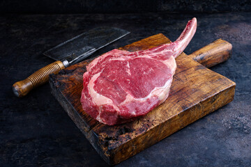 Raw dry aged chianina tomahawk steak offered as close-up with a cleaver on old rustic wooden board