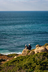 Couple on a cliff looking at waves and the sea in Ericeira, Portugal