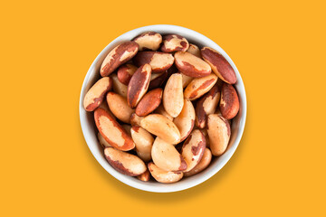Brazil nuts in white bowl with yellow background top view